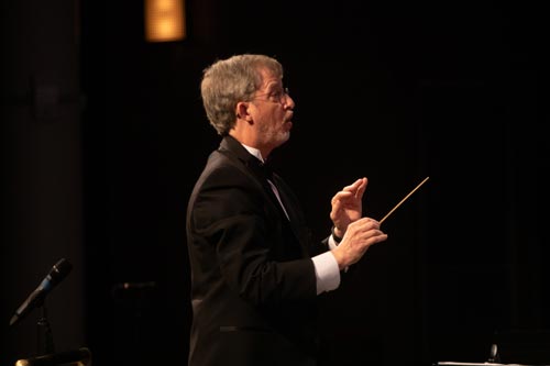 Dr. Doug Harris conducting the Clark College Concert Band ensemble. He is holding a conductor's baton and appears to be in mid-motion on a cue or rhythm. 