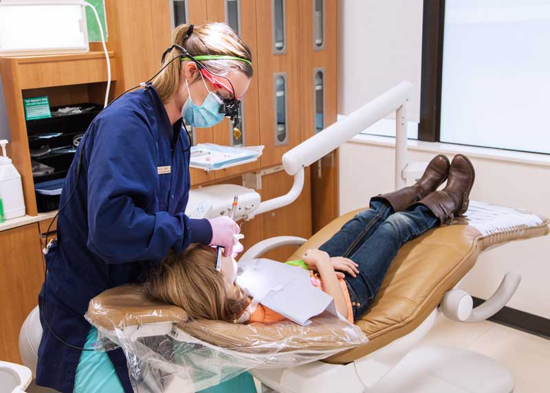 A Clark student hygienist cleaning a child patient's teeth.