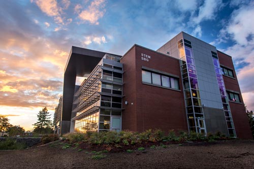 A view of the STEM Building at Clark College with a vibrant sunset in the background, casting a warm glow across the sky